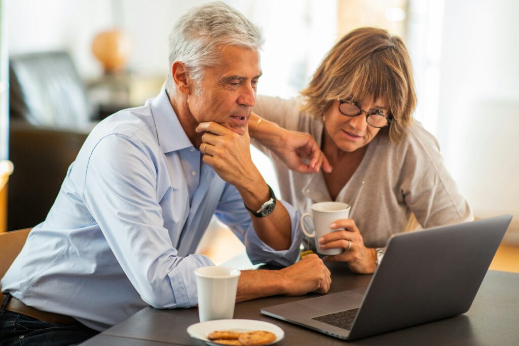 older couple sitting at desk looking at laptop